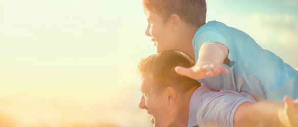 Son on father's shoulders in sunset